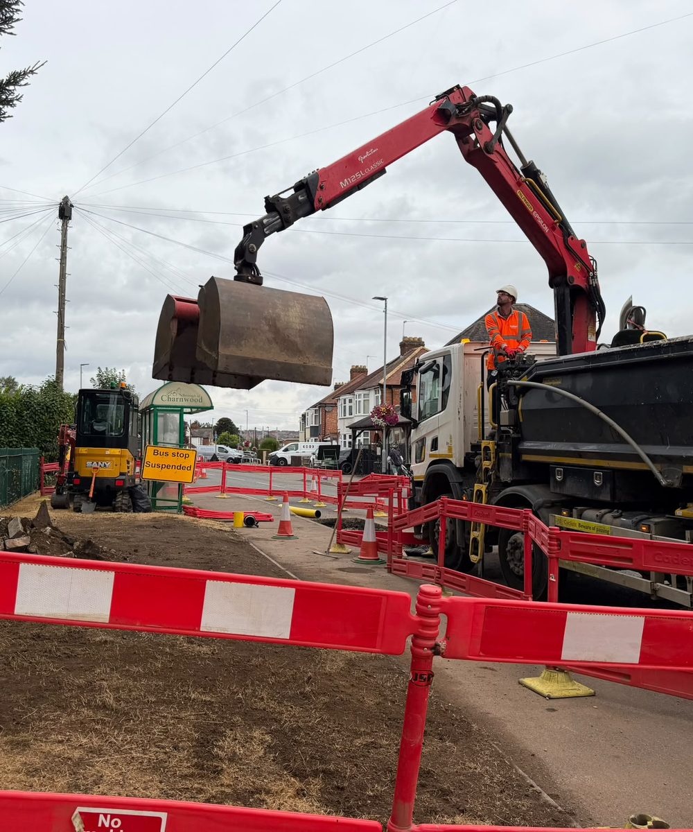 Grab lorry loading spoil from a footway excavation, operator working the crane from the deck