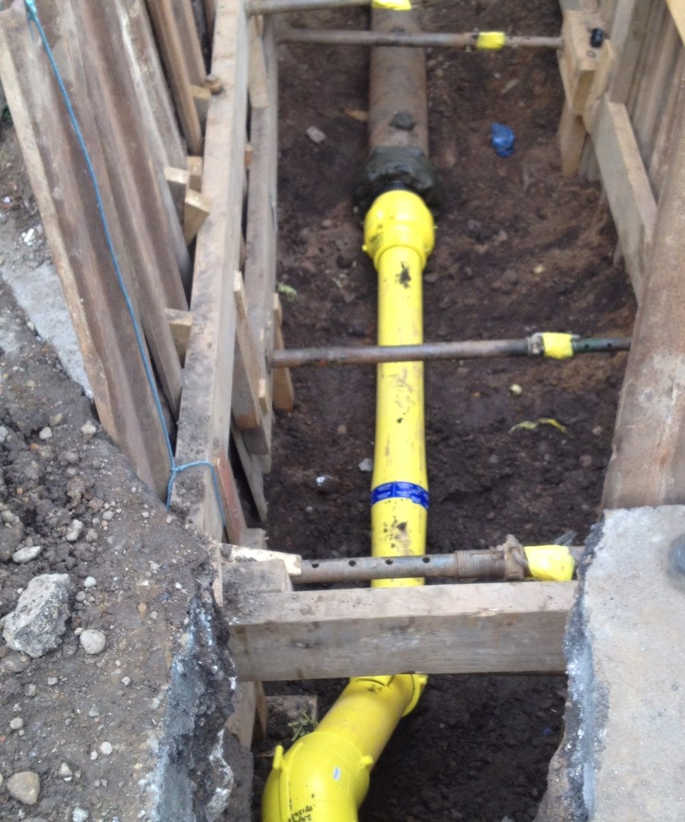 New yellow PE main and service tees laid in a timber-shored trench